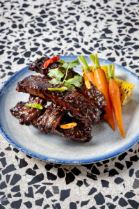 Trang-Stye Pork Ribs: Tender pork ribs marinated in southern Thai spices, festive glaze, baby carrots & grilled sweet corn